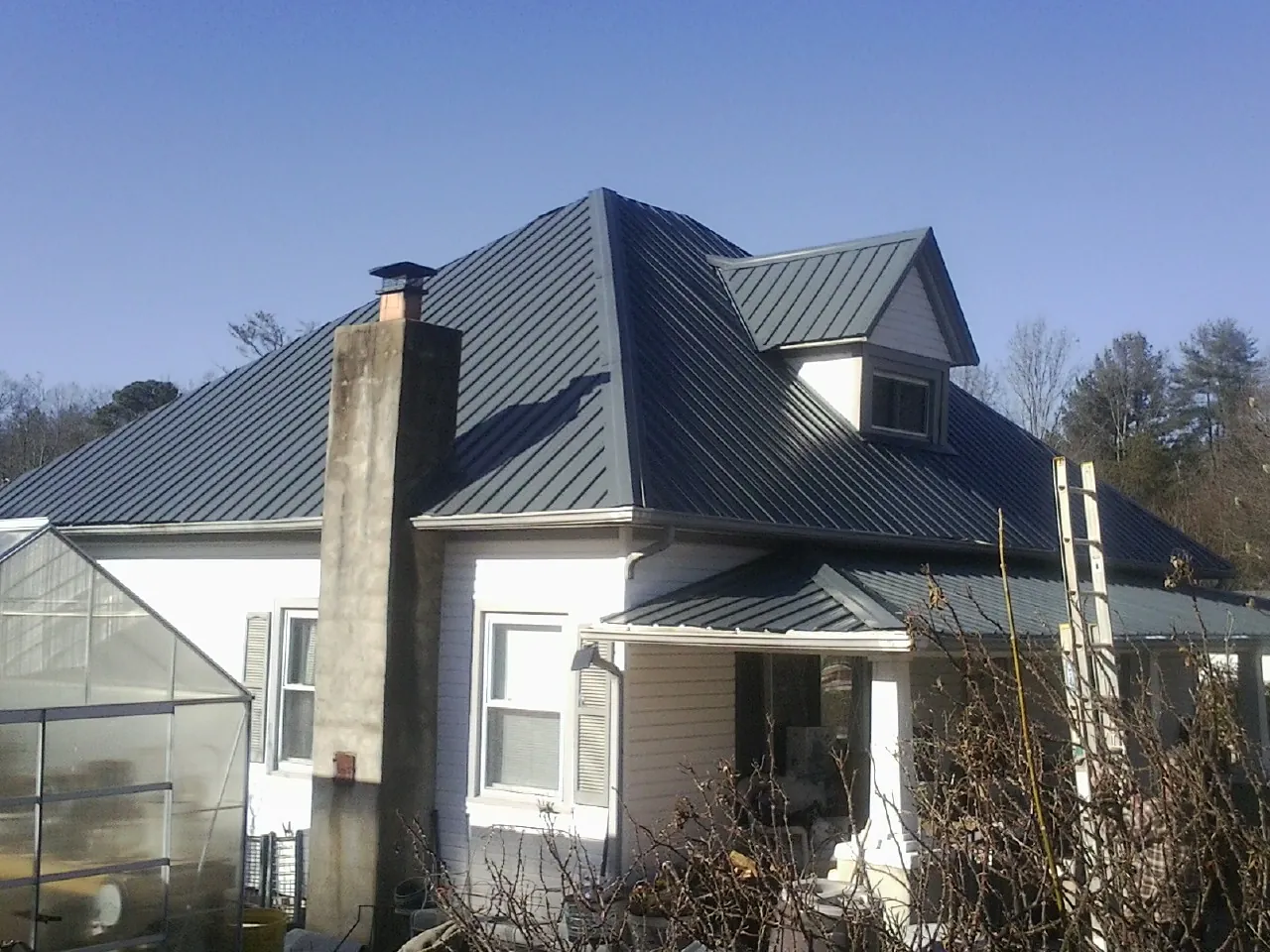 Dark blue standing seam metal roof on a white farmhouse with dormer — Slate & Tile Roof Repair by Roofing Brothers in Delmont