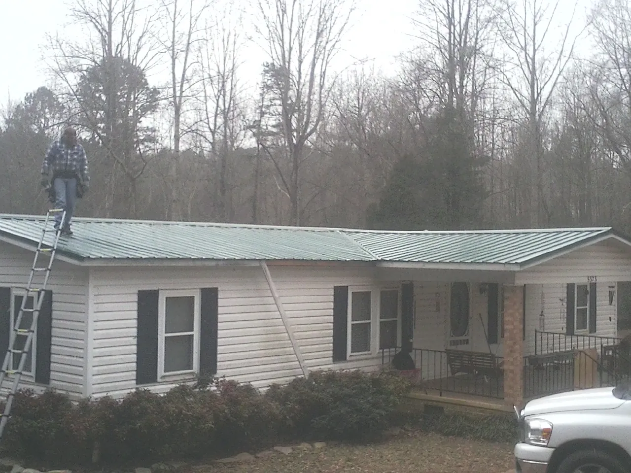Worker on a ladder beside a new green metal roof on a ranch home in Delmont