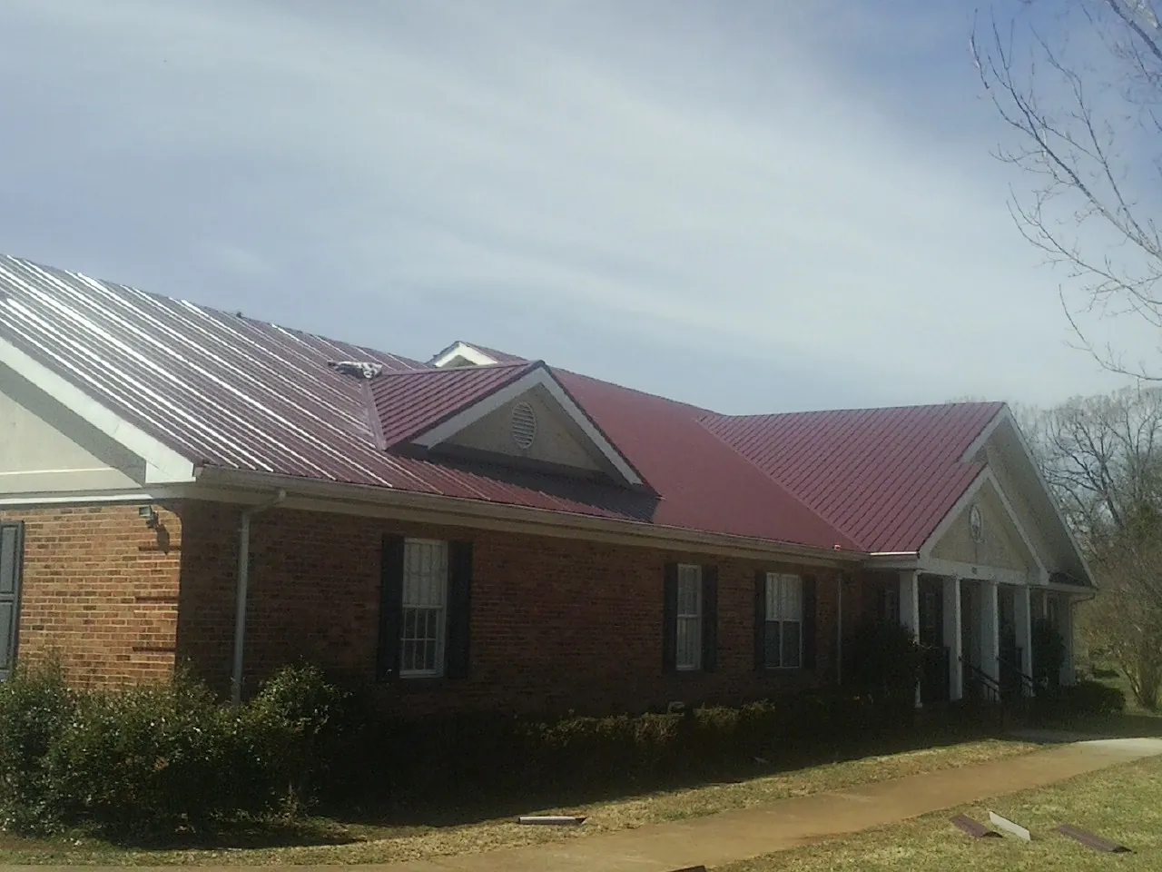 Red metal roof with gabled entries on a long brick building, from a Hail Damage Roof Repair job in Delmont