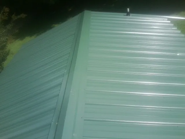 New green metal panels meeting at the ridge of a roof — Flat Roof Repair work by our crew in Delmont