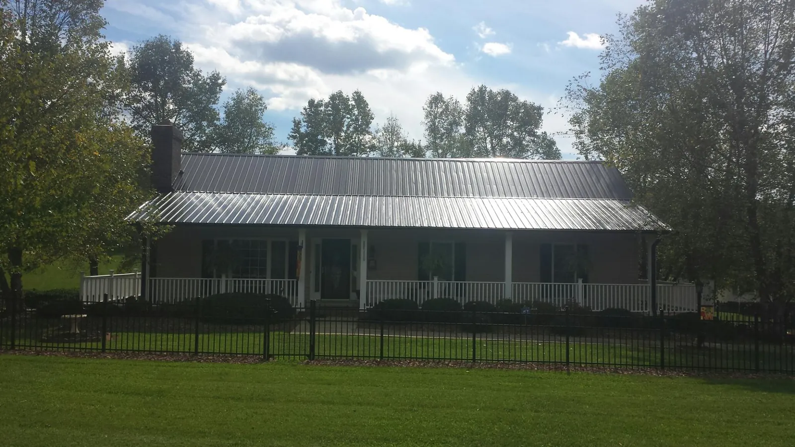 Gray metal roof on a brick ranch with a full width front porch — Gutter Guard Installation work by our crew in Delmont