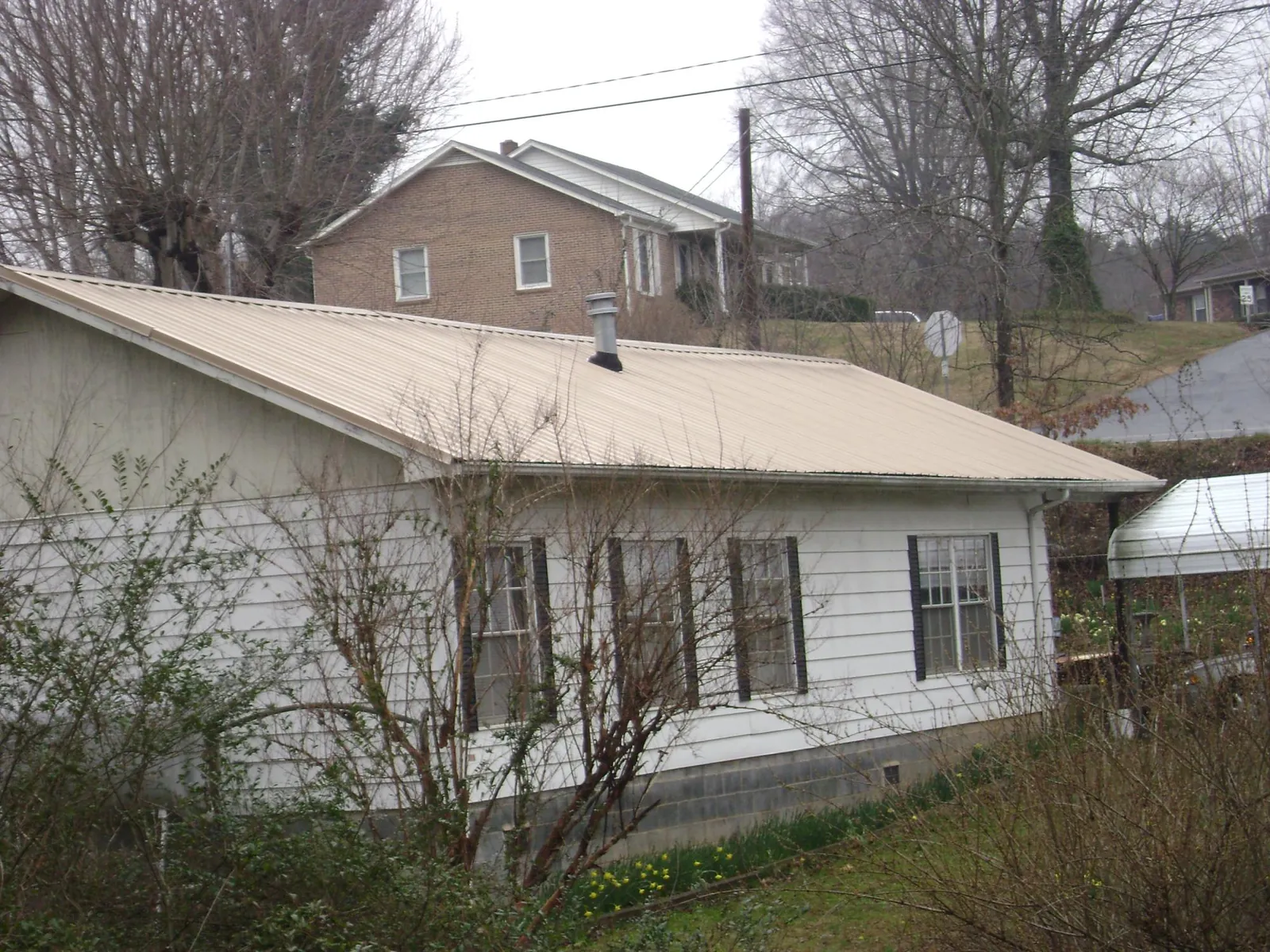 Tan metal roof on a white sided house set into a hillside — Commercial Roofing by Roofing Brothers in Delmont